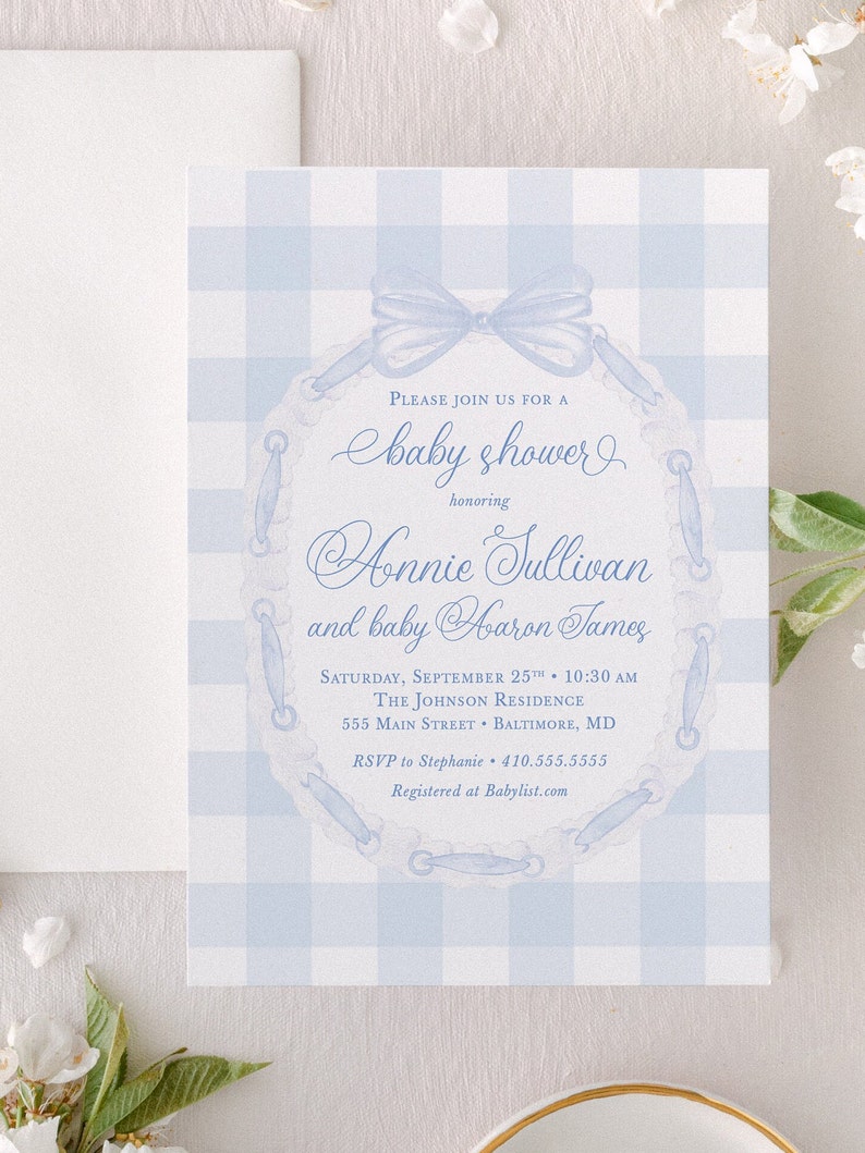 May include: A blue and white gingham baby shower invitation with a blue ribbon and lace design. The invitation reads "Please join us for a baby shower honoring Annie Sullivan and baby Aaron James". The invitation also includes the date, time, location, and RSVP information.