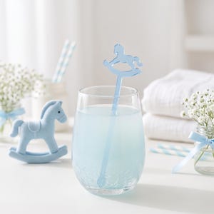 May include: A clear glass tumbler with a crackled texture filled with light blue liquid, featuring a light blue acrylic drink stirrer shaped like a rocking horse. A small, solid light blue rocking horse figurine sits to the left of the glass.