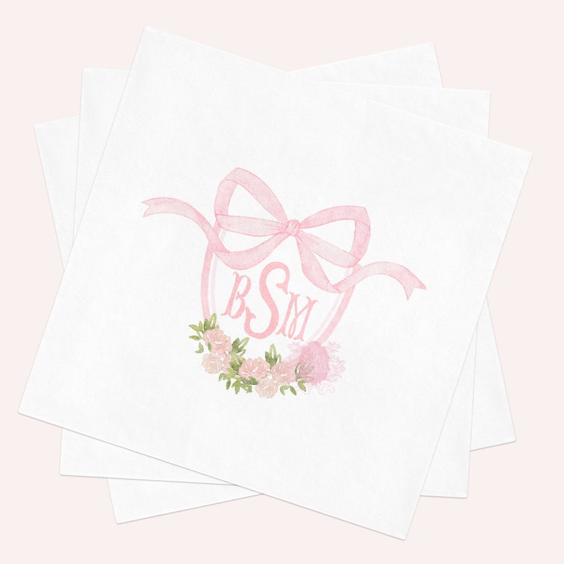 May include: A stack of white square paper napkins featuring a centered watercolor illustration of a pink ribbon bow tied above a pink monogram with the letters BSM, accented by a small cluster of pink roses and green leaves at the bottom.