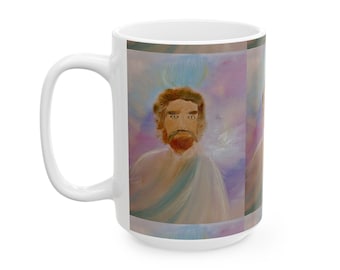 May include: A white ceramic mug featuring a printed illustration of a person with brown hair and a beard, wearing a light-coloured robe. The background of the artwork consists of soft, blended shades of purple, blue, and white, creating a hazy effect.