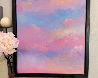 May include: A rectangular painting in a black frame depicting a sky filled with soft, blended clouds in shades of pastel pink, lavender, light blue, and peach. The artwork features a smooth, painterly texture with a gradient of colours across the canvas.