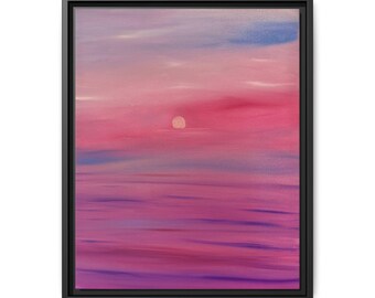 May include: A framed wall art print featuring a horizontal landscape painting of a sunset over water. The scene displays vibrant shades of pink, purple, and magenta with a pale circular sun centred in the sky, all enclosed in a thin black frame.