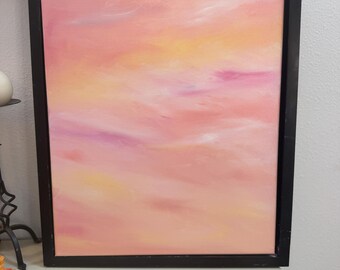 May include: A rectangular canvas painting framed in black, featuring an abstract blend of soft pink, peach, and yellow hues. The colours are applied in smooth, horizontal strokes that create a hazy, cloud-like appearance across the entire surface.