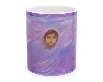 Può includere: Una tazza in ceramica bianca con un'illustrazione dipinta di una persona con capelli castani e barba, centrata su uno sfondo astratto e vorticoso di pennellate nei toni del viola, lavanda e azzurro.