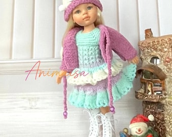 Può includere: Una bambola vestita con un completo lavorato a maglia, tra cui cappello, giacca e vestito. L'abito è una combinazione di blu, viola e bianco. La bambola indossa stivali bianchi. Sullo sfondo c'è una piccola statuina di pupazzo di neve.