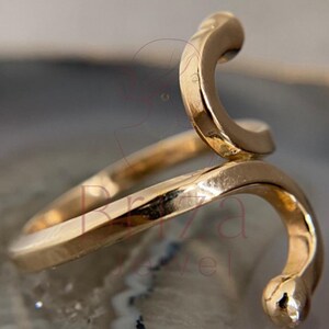 May include: A gold-colored ring in a snake design. The ring wraps around the finger with a curved, stylized snake head and tail. The ring is made of a shiny, metallic material.