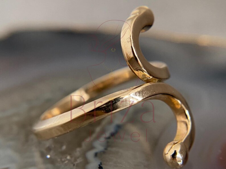 May include: A gold-colored ring in a snake design. The ring wraps around the finger with a curved, stylized snake head and tail. The ring is made of a shiny, metallic material.