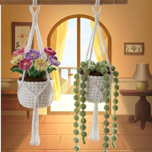 May include: Two white macrame plant hangers. One holds colorful crocheted flowers, the other holds a green, beaded plant. Both are suspended from a wooden rod. The background features a window with yellow curtains and a warm-toned interior.