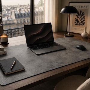 May include: A dark grey rectangular desk mat with a textured surface placed on a wooden desk. The mat features a laptop, a wireless mouse, and a spiral-bound notebook with a pen. The desk mat provides a smooth, flat workspace for office equipment.