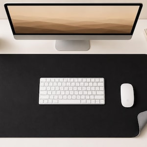 Op de afbeelding: Een grote, rechthoekige zwarte bureauonderlegger met afgeronde hoeken en een glad oppervlak. De mat ligt op een bureau en dient als ondergrond voor een wit draadloos toetsenbord en een witte draadloze computermuis die erop zijn geplaatst.