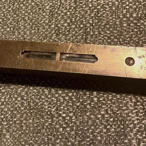 Puede incluir: Un nivel de latón antiguo con dos viales de burbujas. El nivel tiene el texto "WARRANTED No. 1621 CORRECT" y "TAYLOR BROS. SHEFFIELD ENGLAND" grabado. El nivel es rectangular y tiene un aspecto desgastado.