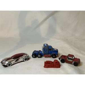 May include: A collection of toy vehicles, including a silver and red sports car, a blue semi-truck, a red flatbed truck, a red fire truck, and a red jeep. The toys are made of plastic and metal.