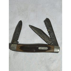May include: A folding pocket knife with two open metal blades showing signs of wear and oxidation. The handle is brown with a textured grip and features a silver-colored metal inlay plate with the embossed text OLD TIMER on the side.