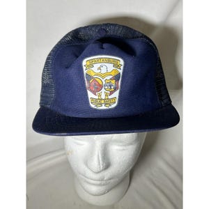 May include: A navy blue trucker hat with a mesh back and a curved brim. The front panel features a patch with the text "SPARTANBURG" above an eagle and the words "PUBLIC SAFETY".