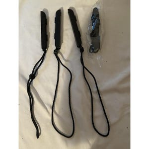 May include: Four black game controller wrist straps. Three are loose, and one is sealed in a clear plastic bag. The straps have a black and white braided design. The controllers are rectangular with a button on the top.