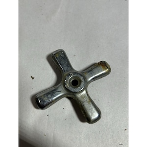 May include: A four-pronged metal faucet handle with a chrome finish. The center of the handle features a circular indentation with the word COLD embossed in capital letters. The surface shows signs of wear, oxidation, and minor rust spots.