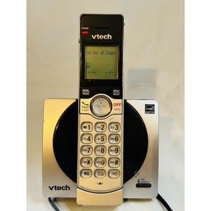 May include: A cordless Vtech phone with a black handset and silver base. The handset displays "no PWR at base" on the screen. Features include a keypad with numbers and function buttons. The base has a circular design.
