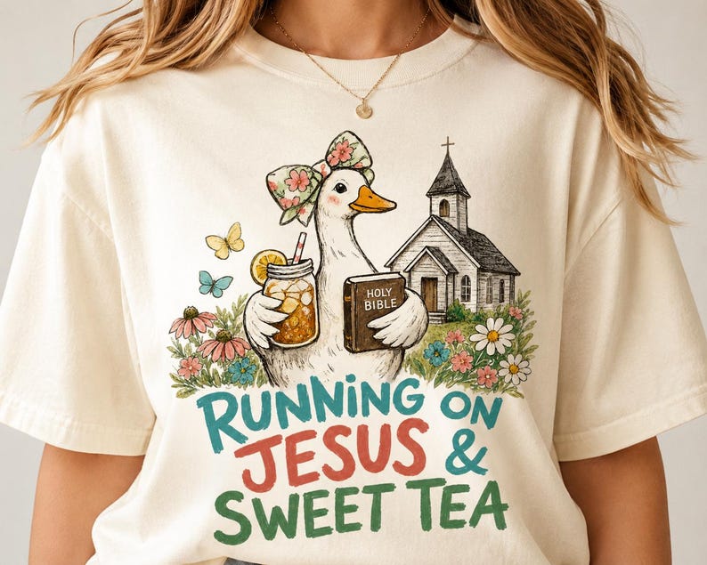 May include: A cream-colored t-shirt featuring a graphic of a duck wearing a floral bow, holding a mason jar of tea and a Holy Bible, standing near a church and flowers. The text reads RUNNING ON JESUS & SWEET TEA in teal and red lettering.