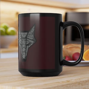 Peut inclure: Un mug en céramique noire avec un panneau rectangulaire rouge foncé sur le côté. Au centre du panneau se trouve un graphique de tête de loup stylisé composé de petits textes blancs, incluant la phrase "BREAK THE CHAINS!" à la verticale.