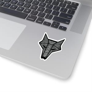 Könnte beinhalten: Ein grauer Aufkleber in Form eines Wolfskopfes mit den Worten "BREAK THE CHAINS" und anderem Text im Design. Der Aufkleber befindet sich auf einem silbernen Laptop.