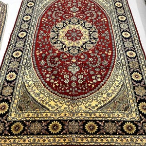 May include: Large, ornate red rug with an oval central design. The rug features a detailed floral pattern in cream, black, and gold. The border is black with floral medallions. The rug has a fringed edge.
