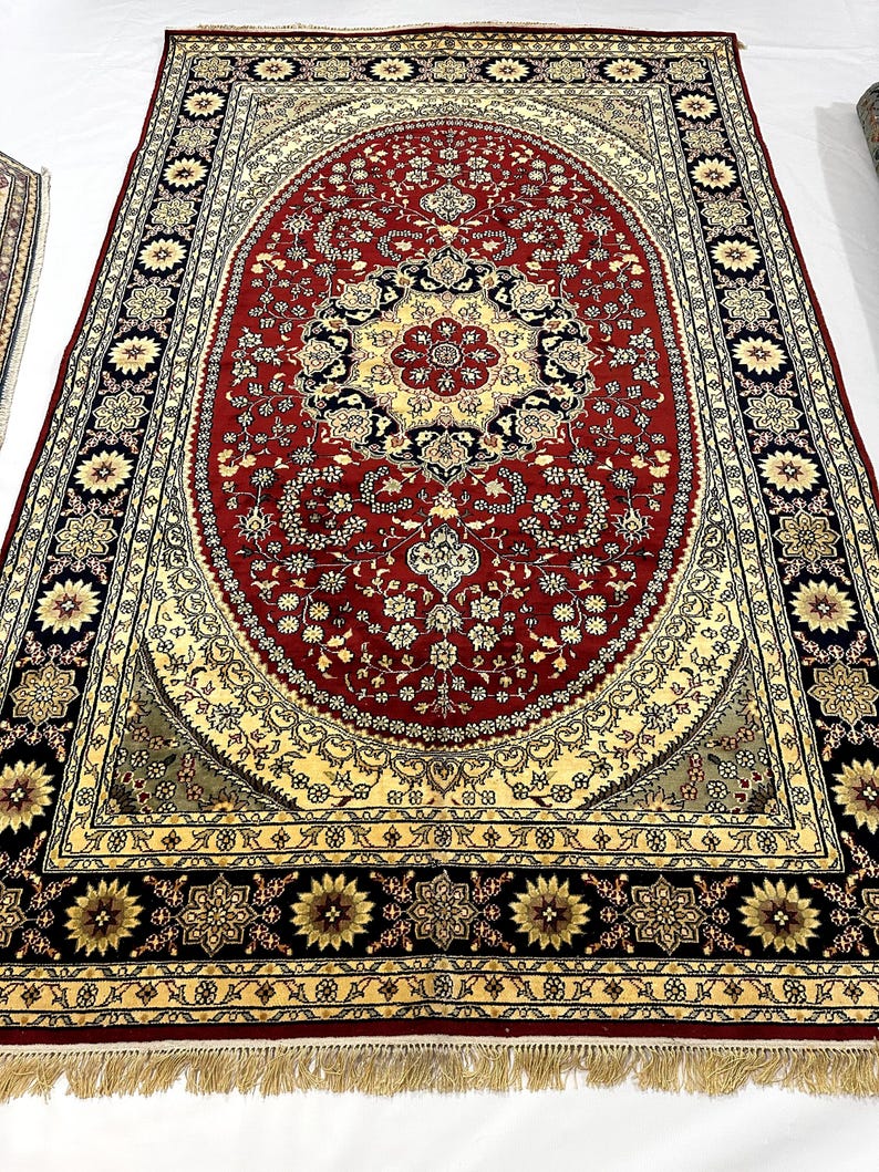 May include: Large, ornate red rug with an oval central design. The rug features a detailed floral pattern in cream, black, and gold. The border is black with floral medallions. The rug has a fringed edge.