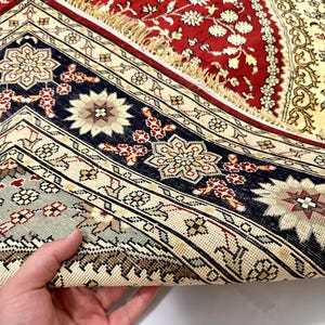 May include: Close-up of a section of a vintage rug with intricate floral patterns. The rug features a rich color palette of red, navy blue, cream, and touches of green. The design includes geometric borders and central floral medallions, showcasing traditional craftsmanship.