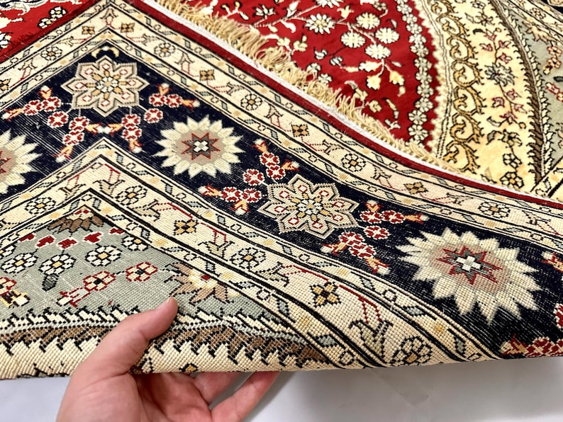 May include: Close-up of a section of a vintage rug with intricate floral patterns. The rug features a rich color palette of red, navy blue, cream, and touches of green. The design includes geometric borders and central floral medallions, showcasing traditional craftsmanship.