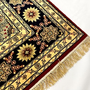 May include: Close-up of a section of an ornate rug with a cream, black, and burgundy color scheme. The rug features floral and geometric patterns, with a fringed edge. The design includes stylized flowers and intricate borders.