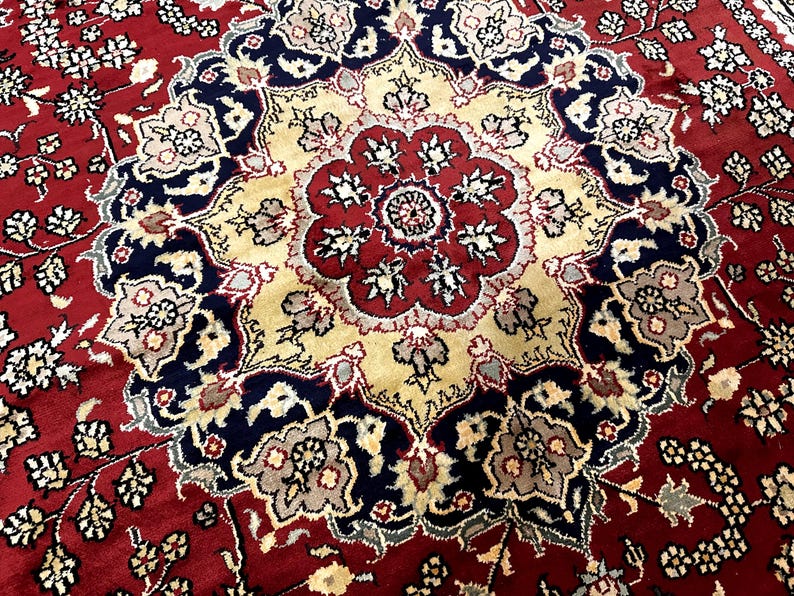 May include: Close-up of a red, beige, and navy blue patterned rug. The rug features a central medallion design with floral and geometric motifs. The border is a deep red with smaller floral patterns.