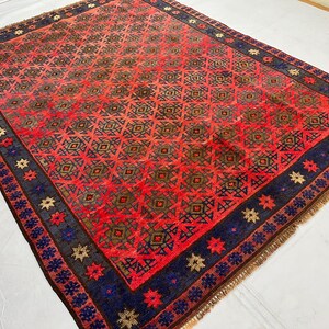 May include: A rectangular area rug featuring a vibrant red field with a repeating dark geometric diamond lattice pattern. The rug is framed by a wide navy blue border decorated with alternating red and beige star-shaped floral motifs and fringe.