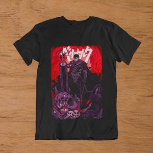 Pode incluir: Uma t-shirt preta de manga curta com uma estampa gráfica de um guerreiro de armadura escura segurando uma espada grande. O design inclui um fundo vermelho vibrante, texto japonês branco e criaturas monstruosas em tons de roxo com caveiras.