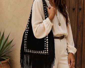 May include: Black suede shoulder bag with silver-tone stud accents and fringe trim. The bag has a rectangular shape and a long shoulder strap. The bag is part of a bohemian style collection.