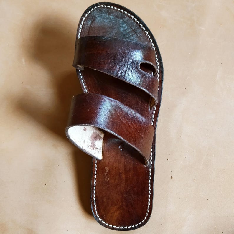 Pu&ograve; includere: Un singolo sandalo in pelle marrone con due cinturini e un bordo bianco cucito. Il sandalo ha una finitura scura e lucida e un design semplice e classico. Il sandalo &egrave; progettato per l'uso casuale.