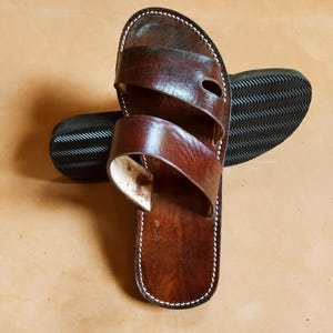 Pu&ograve; includere: Sandali in pelle marrone con due cinturini e cuciture bianche. I sandali hanno una suola marrone scuro con un motivo strutturato. Questi sandali sono progettati per un uso casual.