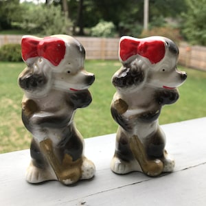May include: A pair of ceramic poodle salt and pepper shakers. The poodles are black and white with red bows and are holding golf clubs.