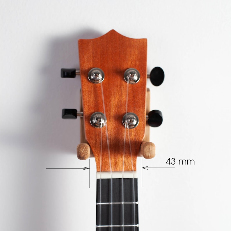 Puede incluir: Primer plano del clavijero de un ukelele. El instrumento de madera tiene un acabado natural con cuatro clavijas y cuerdas. El diapas&oacute;n es negro y el ancho es de 4,3 cm.