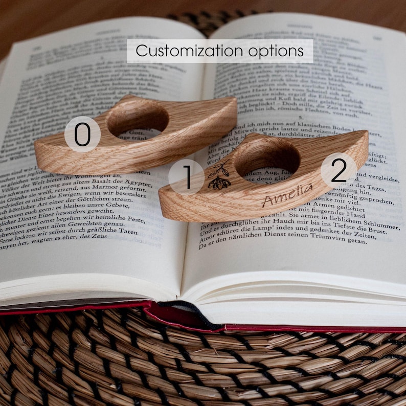 K&ouml;nnte beinhalten: Zwei gebogene Buchst&uuml;tzen aus Holz, die auf einem offenen Buch liegen. Eine hat ein Blumendesign, die andere den Namen "Amelia" eingraviert. Der Text "Customization options" steht oben.