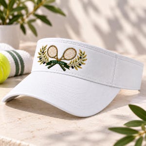 Könnte beinhalten: Ein weißer Sonnenschutz mit einer zentralen Grafik aus zwei gekreuzten Tennisschlägern, die von Olivenzweigen umrahmt sind. Ein dunkelgrünes Banner über den Schlägern trägt den weißen Schriftzug EST. 1966 auf dem Visier.
