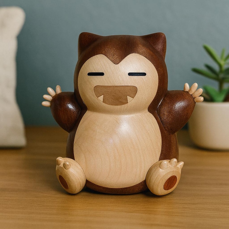 May include: A wooden figurine of a Snorlax character, featuring a light brown belly and limbs, with a darker brown head and back. The figurine has a smiling expression and outstretched arms, and is sitting down. The figurine is on a wooden surface.