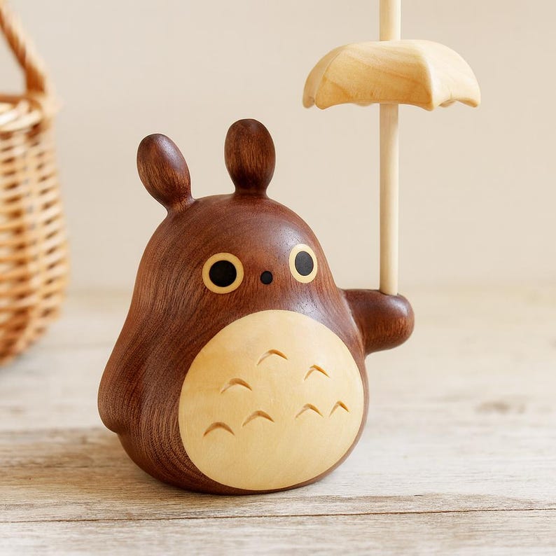 May include: A wooden figurine of a cartoon character with a brown body, large black eyes, and a light-colored belly. The character holds a small, light-colored wooden umbrella. The figurine is on a wooden surface.