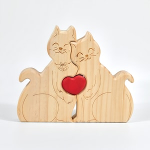 May include: Wooden puzzle featuring two cat figures embracing a red heart. The cats are light brown with etched details, including smiling faces and a bell design. The puzzle is designed to interlock, symbolizing unity and love.
