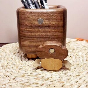 May include: A wooden desk organizer with a matching mushroom-shaped magnet. The organizer is a dark brown color and holds several pens. The mushroom magnet is light brown and tan. The organizer and magnet are on a woven mat.