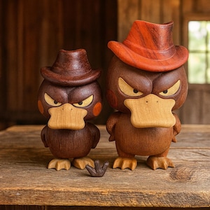 Könnte beinhalten: Zwei Holz-Entenfiguren mit Cowboyhüten. Die Enten haben wütende Ausdrücke mit gelben Augen und orangefarbenen Wangenflecken. Die Hüte sind rotbraun. Eine kleine Holz-Klaue liegt vor den Enten.