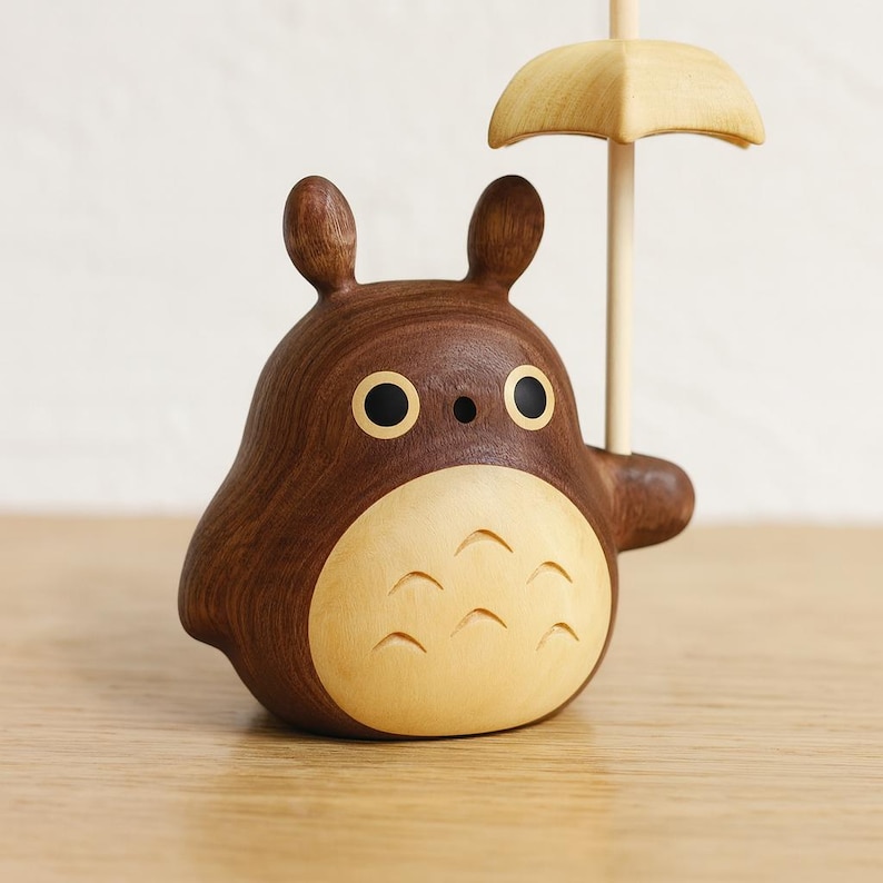 May include: A wooden figurine of a cartoon character with a brown body and a light-colored belly. The character has large black eyes and is holding a small, light-colored umbrella. The figurine is made of wood and has a smooth finish.