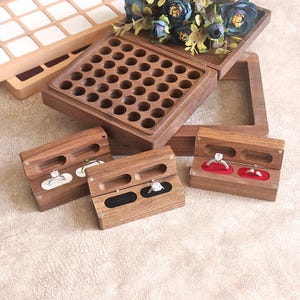 Könnte beinhalten: Holzschmuckkästchen in verschiedenen Größen und Designs. Die Kästchen sind aus dunklem Holz gefertigt und verfügen über Fächer für Ringe und anderen Schmuck. Einige Kästchen haben ein rotes oder schwarzes Samtfutter. Eine größere Box mit mehreren kreisförmigen Löchern ist ebenfalls sichtbar.