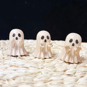 Könnte beinhalten: Drei Holzgeister-Figuren mit schwarzen Augen- und Munddetails. Jeder Geist hat eine einzigartige Handgeste, die aus hellem Holz geschnitzt wurde. Die Geister stehen auf einer gewebten Oberfläche mit dunklem Hintergrund.