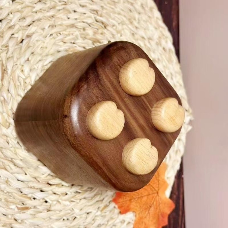 May include: A handcrafted wooden box with a rich, dark brown finish. The top of the box features four light-colored, rounded knobs. The box is set against a woven, beige background, with a hint of an orange leaf.