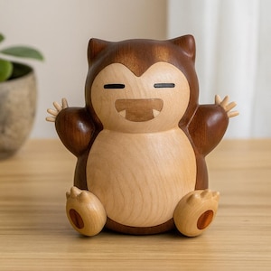 May include: A wooden Snorlax figurine, featuring a light brown body and dark brown accents. The figurine has a smiling expression with small arms and feet outstretched. The handcrafted design showcases the natural wood grain.