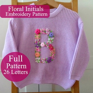 Könnte beinhalten: Ein hellvioletter Rippstrickpullover mit einem großen Buchstaben B, der mit bunten Blumenmotiven bestickt ist. Der Text auf dem Bild lautet Floral Initials Embroidery Pattern und Full Pattern 26 Letters. Der Pullover hängt auf einem Holzkleiderbügel.